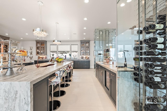 kitchen featuring decorative light fixtures, light tile flooring, light stone countertops, a large island, and sink