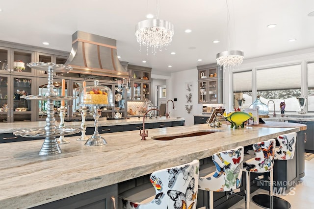 kitchen featuring gray cabinets, decorative light fixtures, a notable chandelier, and light stone counters