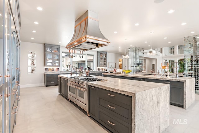 kitchen featuring light stone countertops, decorative light fixtures, premium range hood, double oven range, and a large island