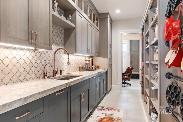 kitchen featuring light stone countertops, gray cabinetry, backsplash, light tile floors, and sink