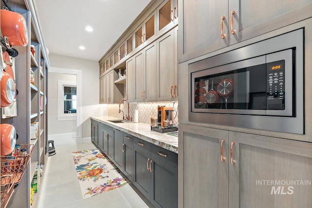 kitchen featuring light stone countertops, stainless steel microwave, tasteful backsplash, sink, and light tile floors