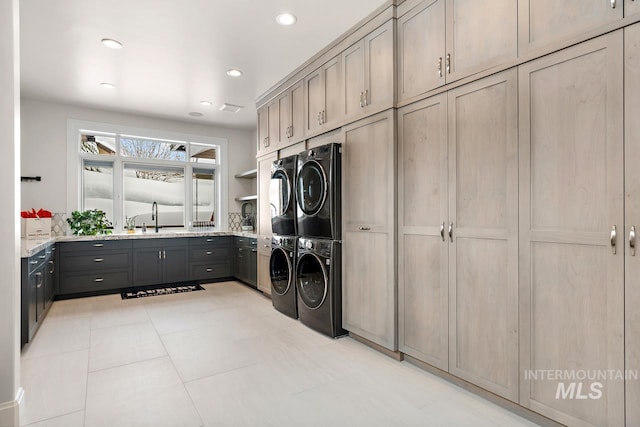 clothes washing area featuring sink, cabinets, light tile floors, and stacked washer / drying machine