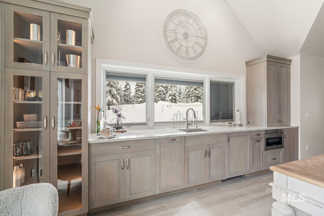 kitchen featuring lofted ceiling, sink, light stone countertops, and oven