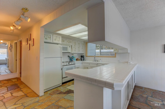 kitchen featuring a textured ceiling, white appliances, light tile patterned floors, tile counters, and track lighting