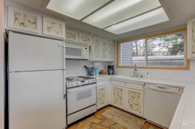 kitchen with white appliances, tile countertops, sink, light tile patterned floors, and decorative backsplash