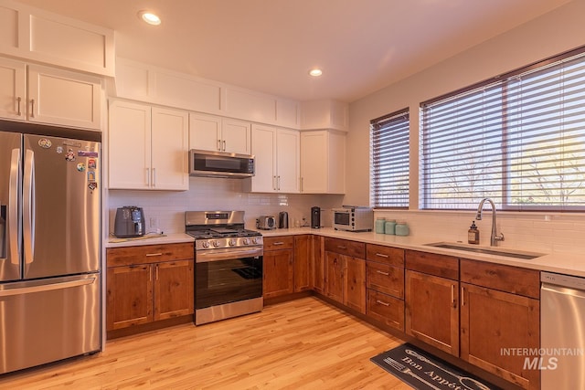 kitchen featuring tasteful backsplash, stainless steel appliances, light countertops, white cabinetry, and a sink