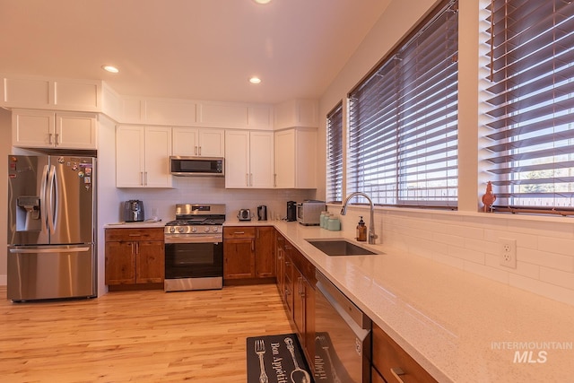 kitchen with light stone counters, brown cabinets, stainless steel appliances, white cabinetry, and a sink