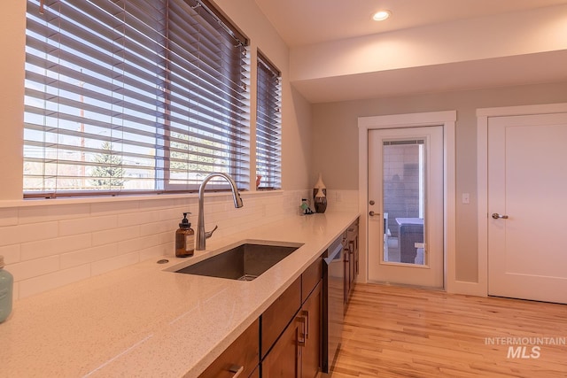 kitchen with light wood finished floors, tasteful backsplash, a sink, light stone countertops, and dishwasher