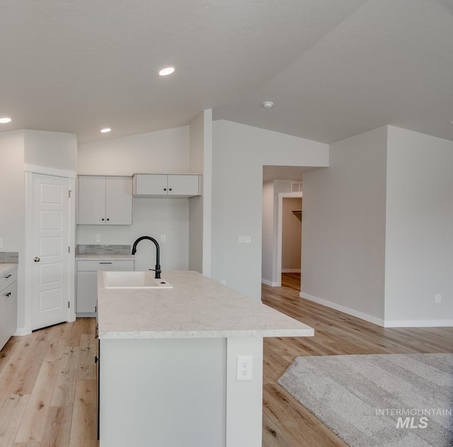 kitchen featuring white cabinetry, vaulted ceiling, sink, and a kitchen island with sink