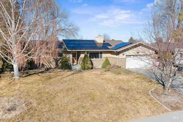 single story home featuring brick siding, a chimney, roof mounted solar panels, a garage, and a front lawn