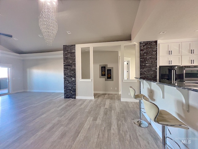 kitchen with an inviting chandelier, light hardwood / wood-style flooring, dark stone countertops, a breakfast bar area, and white cabinets