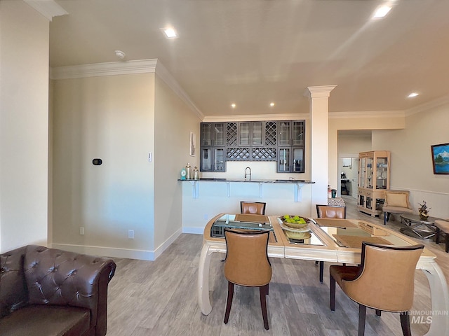 dining room with wet bar, ornamental molding, ornate columns, and light hardwood / wood-style flooring