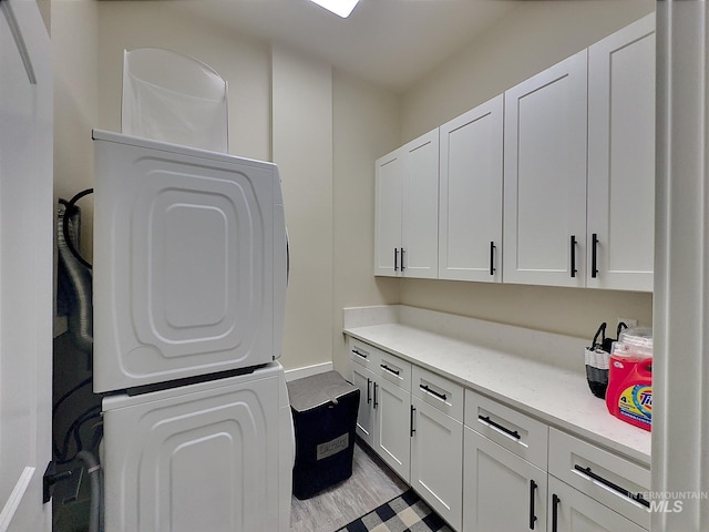 laundry room featuring cabinets, stacked washing maching and dryer, and light wood-type flooring