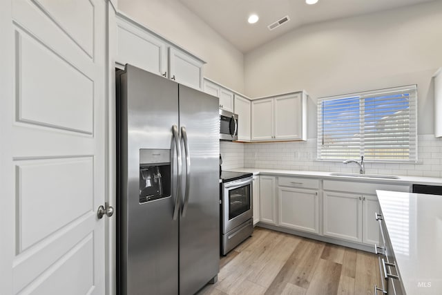 kitchen with light wood finished floors, light countertops, decorative backsplash, stainless steel appliances, and a sink