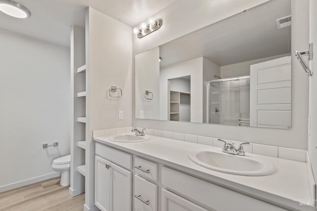 bathroom featuring wood finished floors, a stall shower, toilet, and a sink