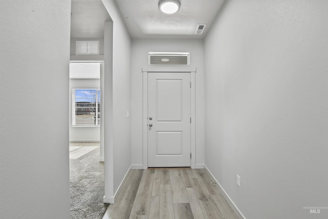 hallway featuring visible vents, light wood-style floors, and baseboards