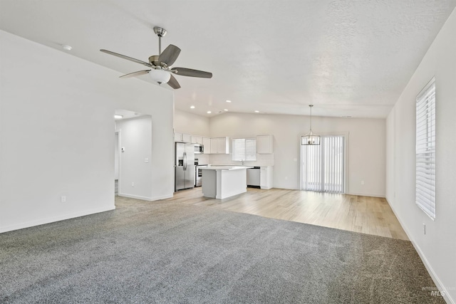 unfurnished living room featuring baseboards, lofted ceiling, a textured ceiling, light carpet, and ceiling fan with notable chandelier