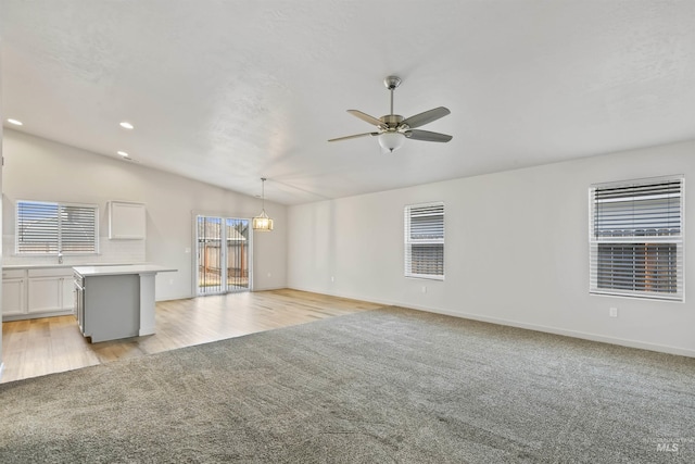 unfurnished living room with ceiling fan, baseboards, lofted ceiling, light carpet, and recessed lighting