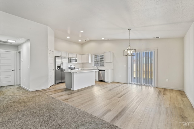 kitchen featuring light countertops, vaulted ceiling, appliances with stainless steel finishes, white cabinetry, and a center island