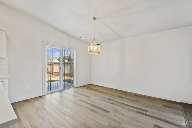 unfurnished dining area featuring baseboards, lofted ceiling, a notable chandelier, and light wood-style flooring