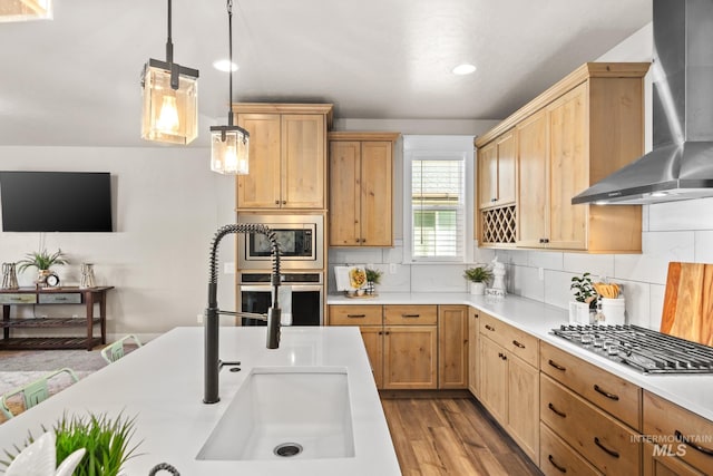 kitchen featuring pendant lighting, sink, wall chimney range hood, stainless steel appliances, and light hardwood / wood-style floors