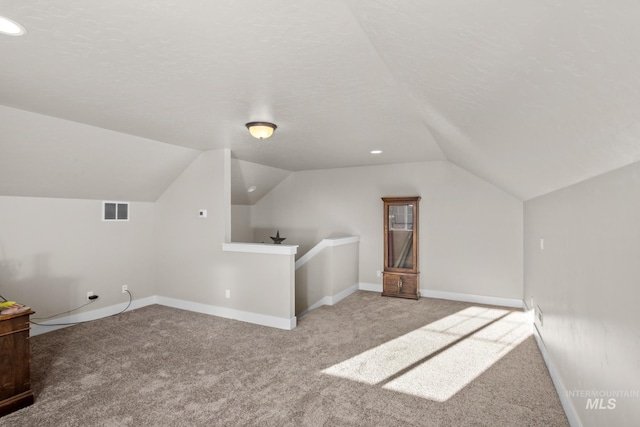 bonus room featuring vaulted ceiling, a textured ceiling, and light colored carpet