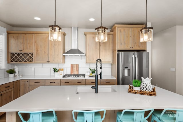 kitchen with appliances with stainless steel finishes, decorative backsplash, an island with sink, a breakfast bar area, and wall chimney range hood