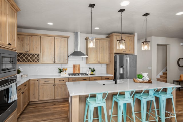 kitchen featuring appliances with stainless steel finishes, a center island with sink, wall chimney exhaust hood, and pendant lighting