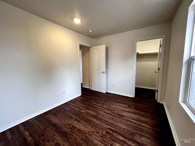 unfurnished bedroom with a walk in closet, dark wood-type flooring, and a closet