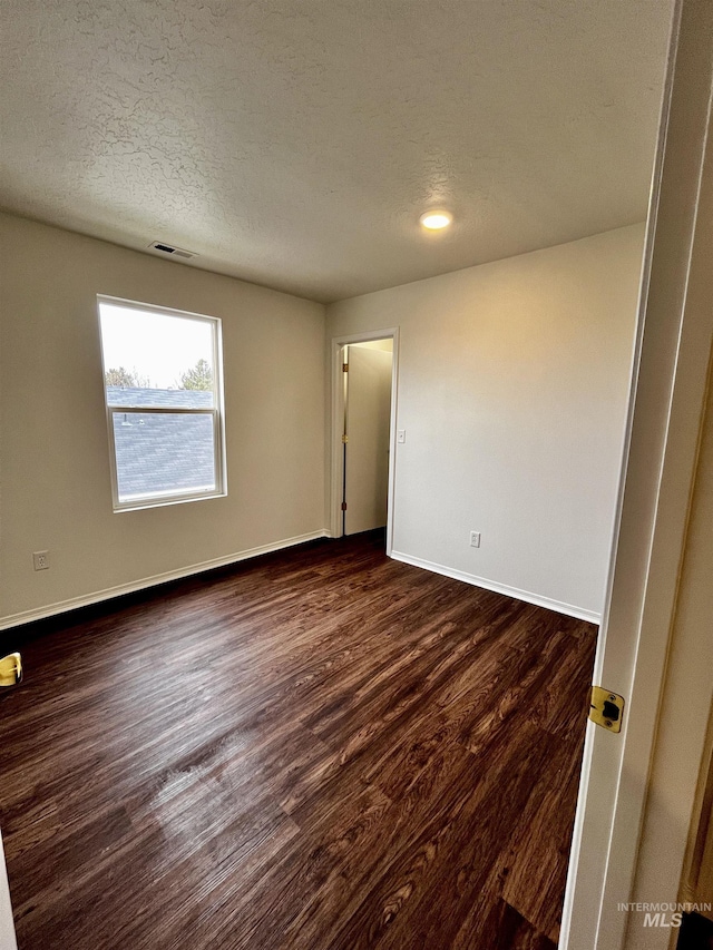 unfurnished room featuring dark wood-type flooring and a textured ceiling