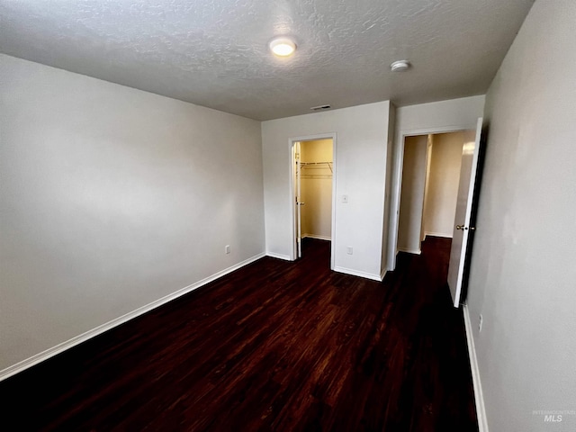 unfurnished bedroom with a walk in closet, dark wood-type flooring, a textured ceiling, and a closet