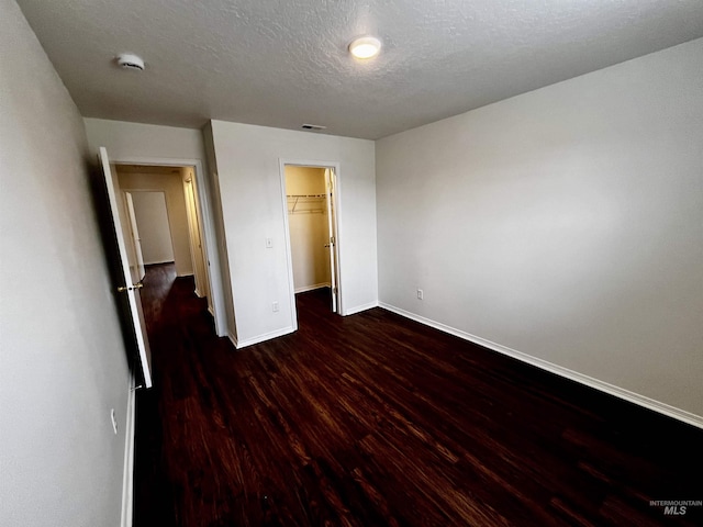 unfurnished bedroom featuring a spacious closet, dark wood-type flooring, a closet, and a textured ceiling