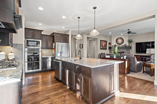 kitchen with an island with sink, appliances with stainless steel finishes, decorative backsplash, pendant lighting, and sink