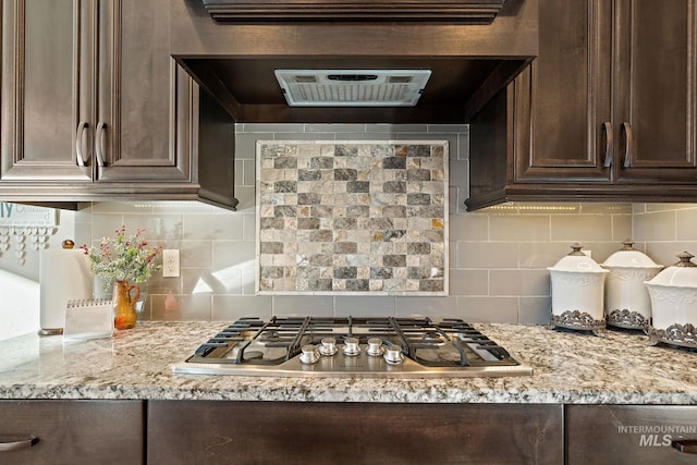 kitchen featuring tasteful backsplash, stainless steel gas cooktop, light stone counters, and dark brown cabinetry