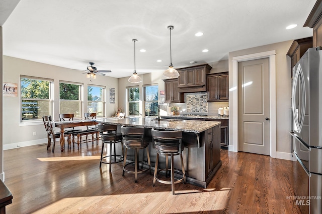 kitchen featuring stainless steel appliances, decorative backsplash, a kitchen island with sink, decorative light fixtures, and light stone countertops