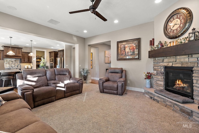 living room featuring ceiling fan, light carpet, sink, and a stone fireplace