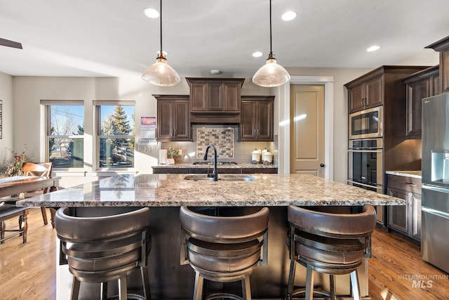 kitchen with hanging light fixtures, stainless steel appliances, and a kitchen island with sink