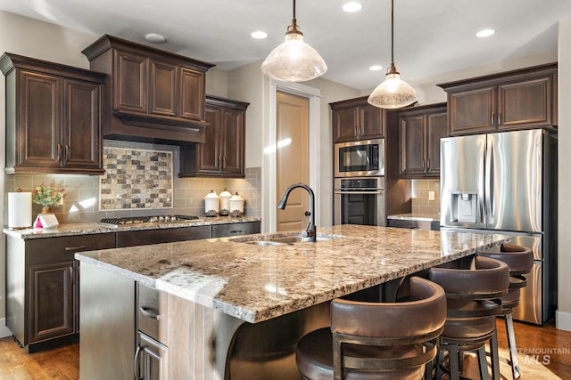 kitchen with backsplash, appliances with stainless steel finishes, sink, and a center island with sink