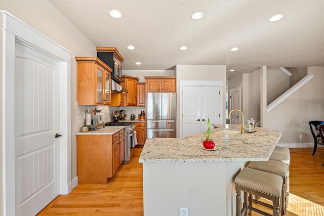 kitchen featuring sink, an island with sink, stainless steel appliances, and light hardwood / wood-style floors