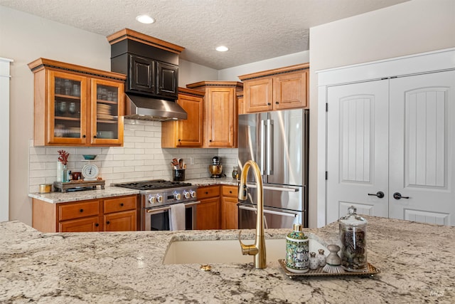 kitchen featuring tasteful backsplash, light stone countertops, stainless steel appliances, and a textured ceiling