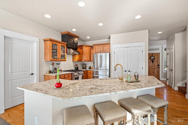 kitchen featuring stainless steel appliances, light stone counters, a large island with sink, a breakfast bar area, and light wood-type flooring