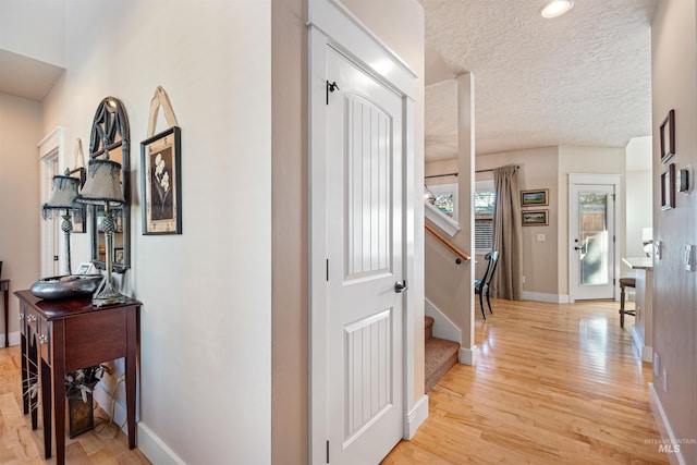 hall with a textured ceiling and light hardwood / wood-style flooring