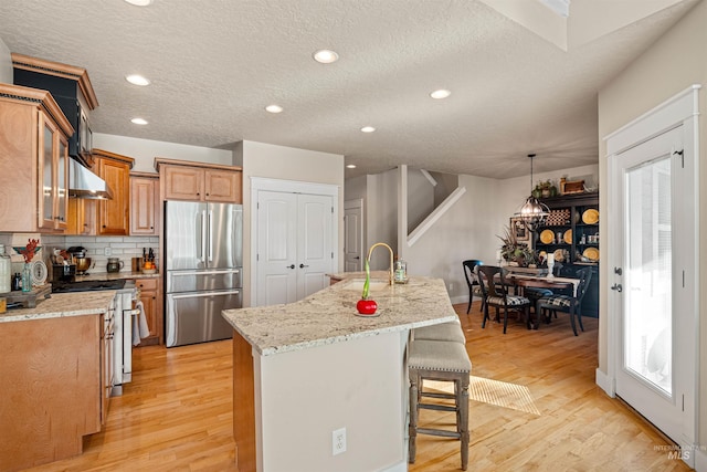 kitchen featuring stainless steel refrigerator, light stone countertops, range with electric cooktop, light hardwood / wood-style flooring, and a kitchen island with sink