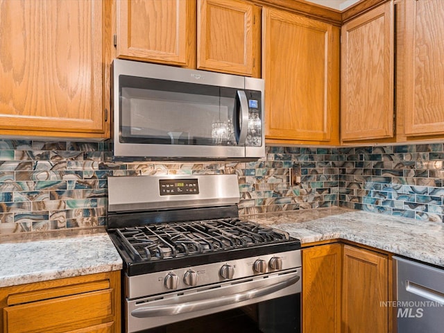 kitchen featuring stainless steel appliances, light stone countertops, and decorative backsplash