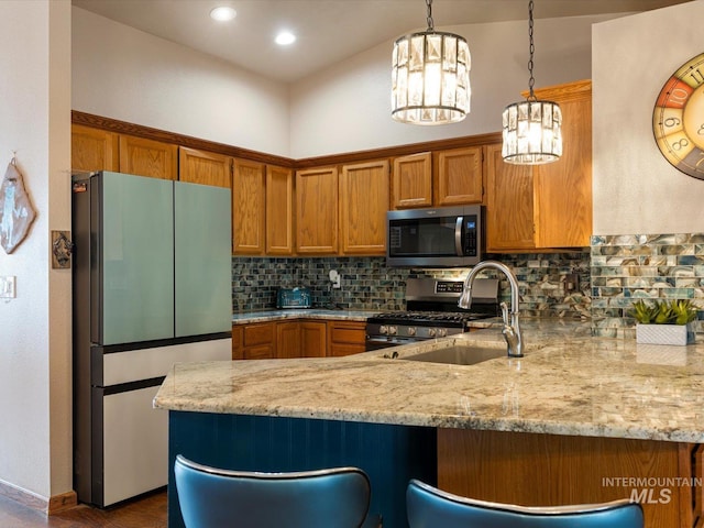 kitchen with hanging light fixtures, sink, tasteful backsplash, light stone countertops, and appliances with stainless steel finishes