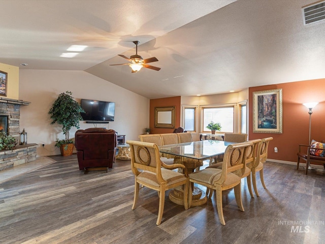 dining area with a stone fireplace, dark hardwood / wood-style floors, ceiling fan, and vaulted ceiling