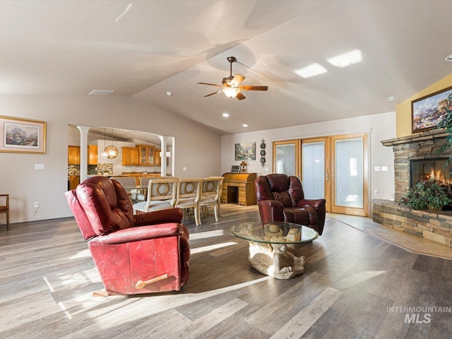 living room featuring a stone fireplace, hardwood / wood-style floors, lofted ceiling, and ornate columns