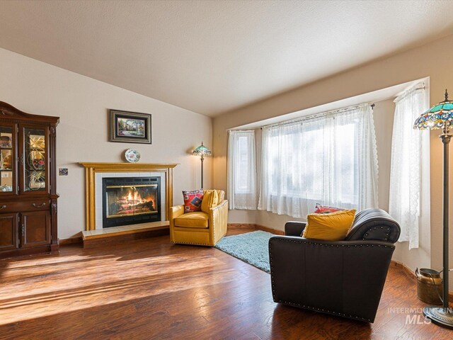 living area with hardwood / wood-style flooring, a tile fireplace, and vaulted ceiling