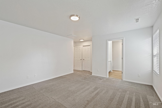 carpeted spare room with visible vents, a textured ceiling, and baseboards