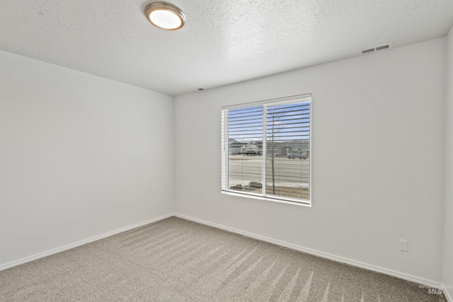 spare room featuring carpet, visible vents, a textured ceiling, and baseboards